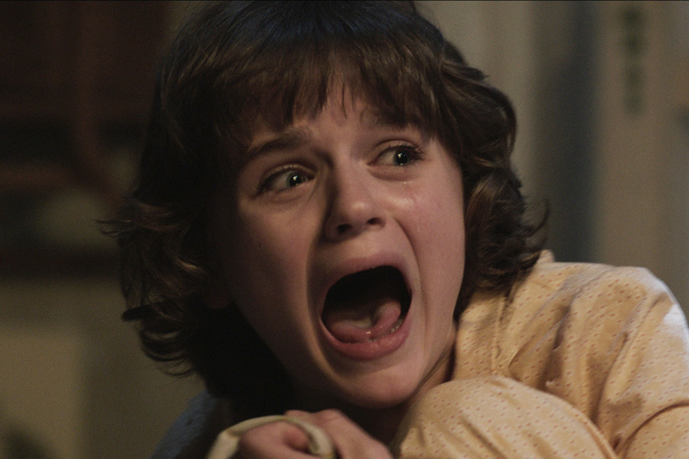 A frightened young girl with curly brown hair screams and cries in a close-up scene from The Conjuring.
