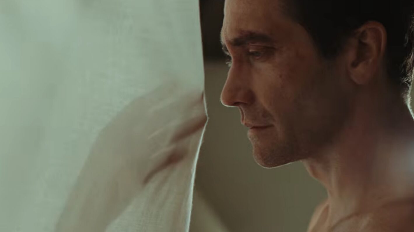 Close-up profile of a dark-haired shirtless man pressing his face against a white fabric surface, eyes downcast.