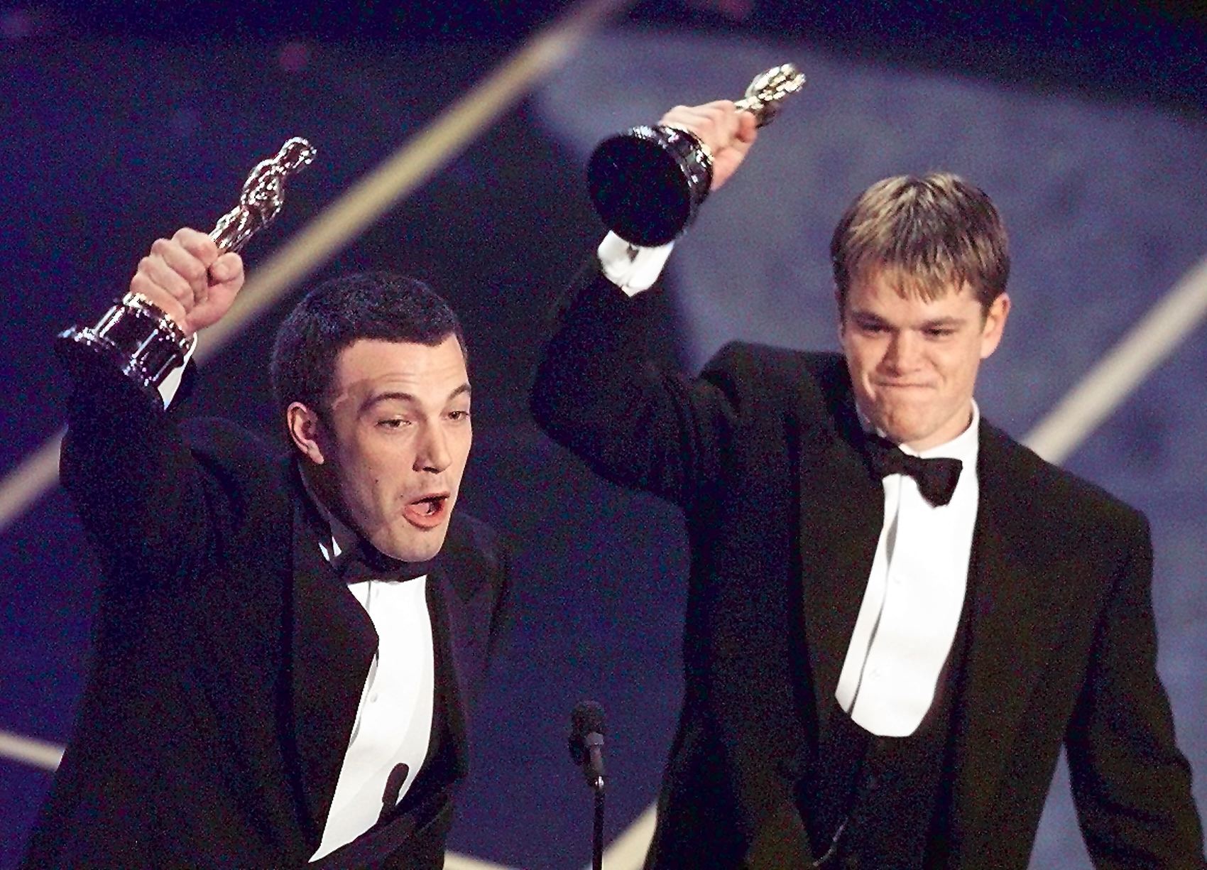 Ben Affleck and Matt Damon holding up their Oscar statuettes after winning Best Original Screenplay for Good Will Hunting at the 70th Academy Awards