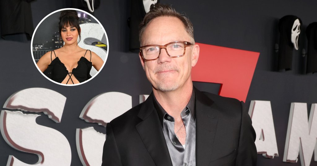 Matthew Lillard in a black suit and silver satin shirt at the Scream 7 premiere, standing in front of a backdrop featuring Ghostface masks.