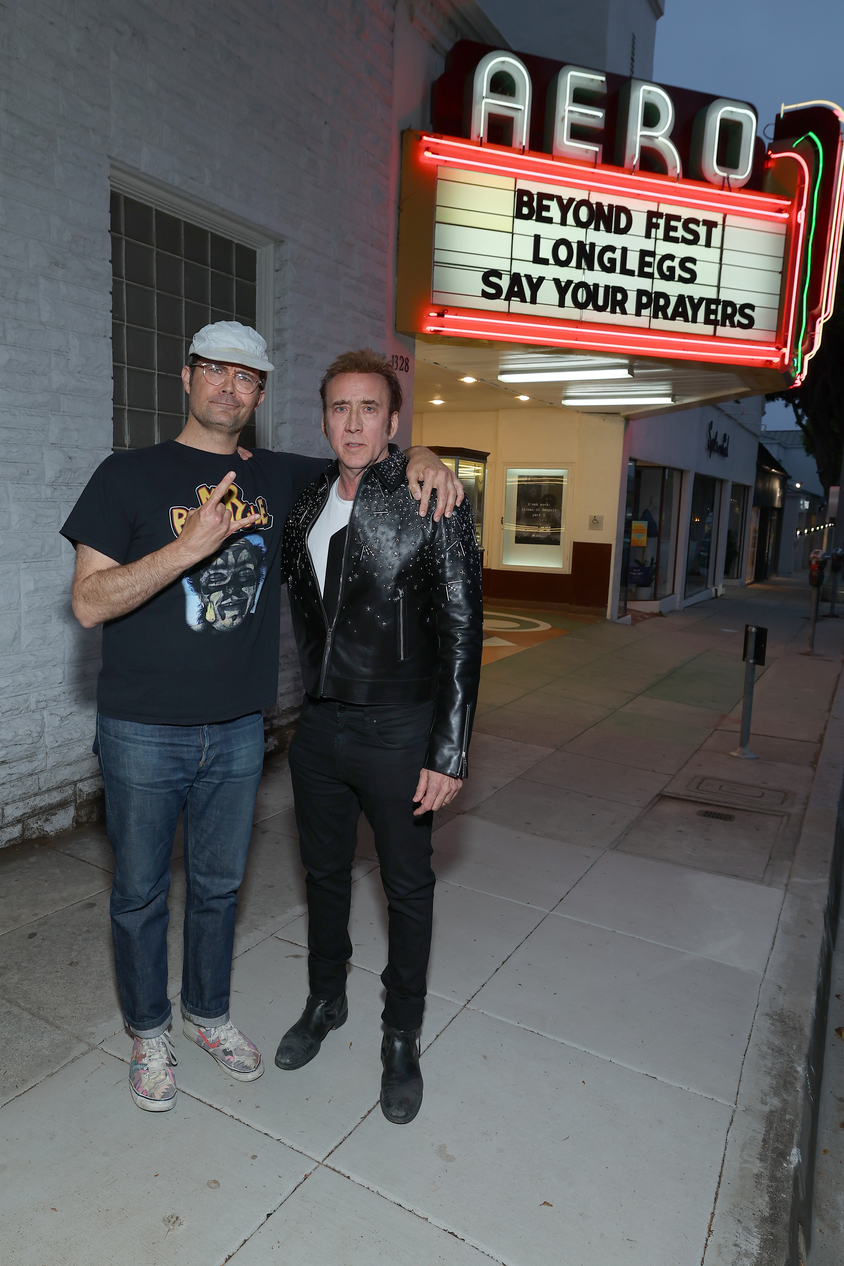 Two men pose on a sidewalk beneath an Aero Theatre marquee reading 'Beyond Fest / Longlegs / Say Your Prayers' at dusk.