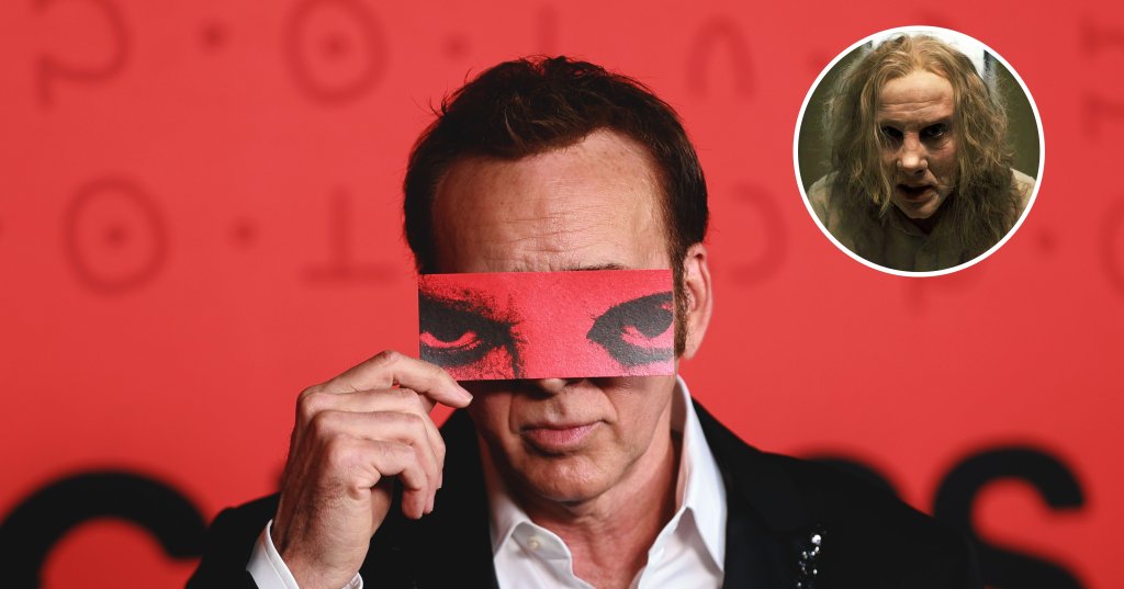 Man in black blazer holding a red card with printed eyes over his face at a movie premiere, standing in front of a red backdrop.
