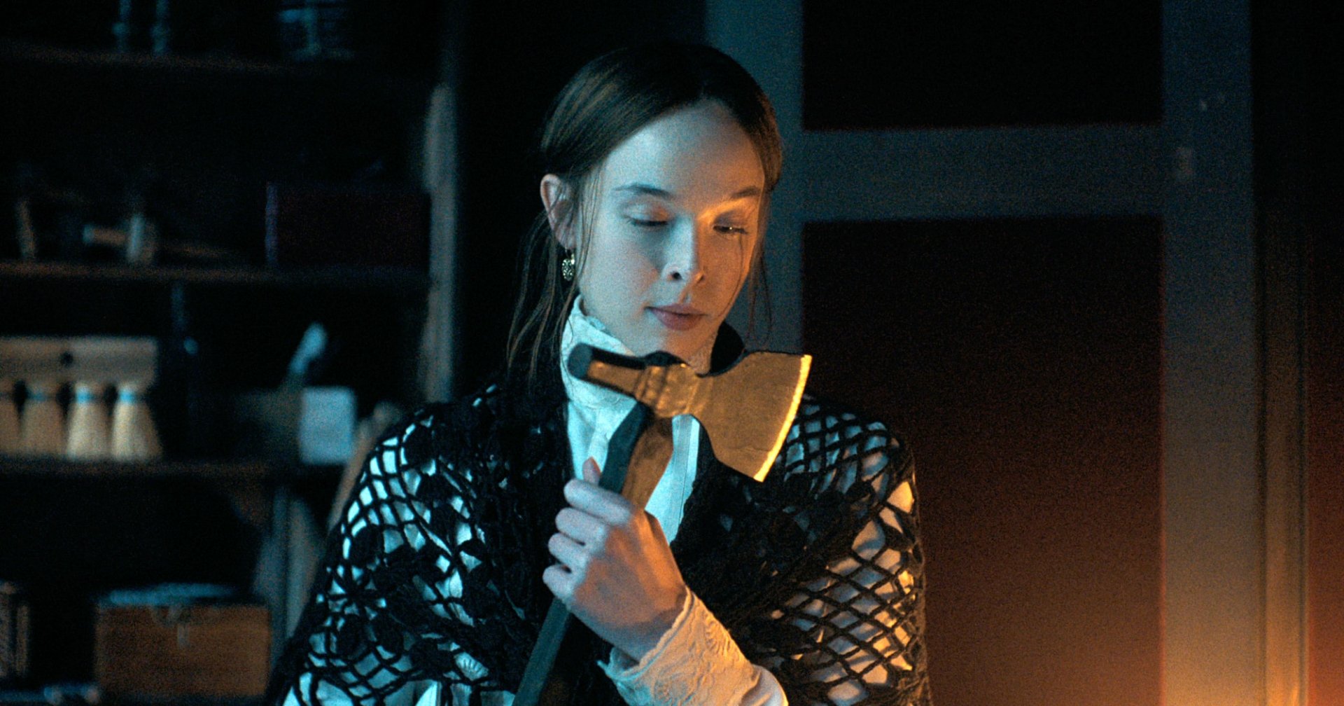 A young woman in a white blouse and black net shawl holds an axe and gazes downward in a dimly lit room.