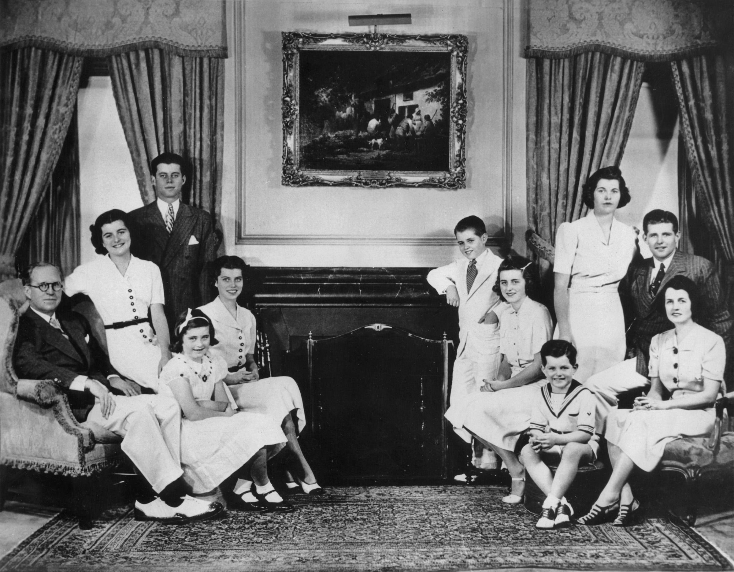 Black-and-white indoor portrait of the Kennedy family — parents and all nine children — seated and standing in an elegantly decorated room with a fireplace, 1937.