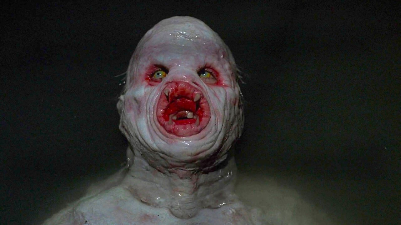 A pale, bald humanoid creature with deeply wrinkled skin, glowing yellow eyes, and a circular lamprey-like mouth full of teeth, against a dark background.