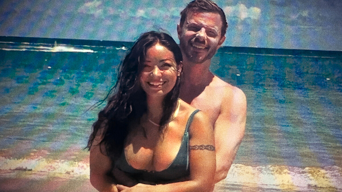 Smiling man and woman embracing on a beach in swimwear, photographed in a faded, aged style with ocean in the background.