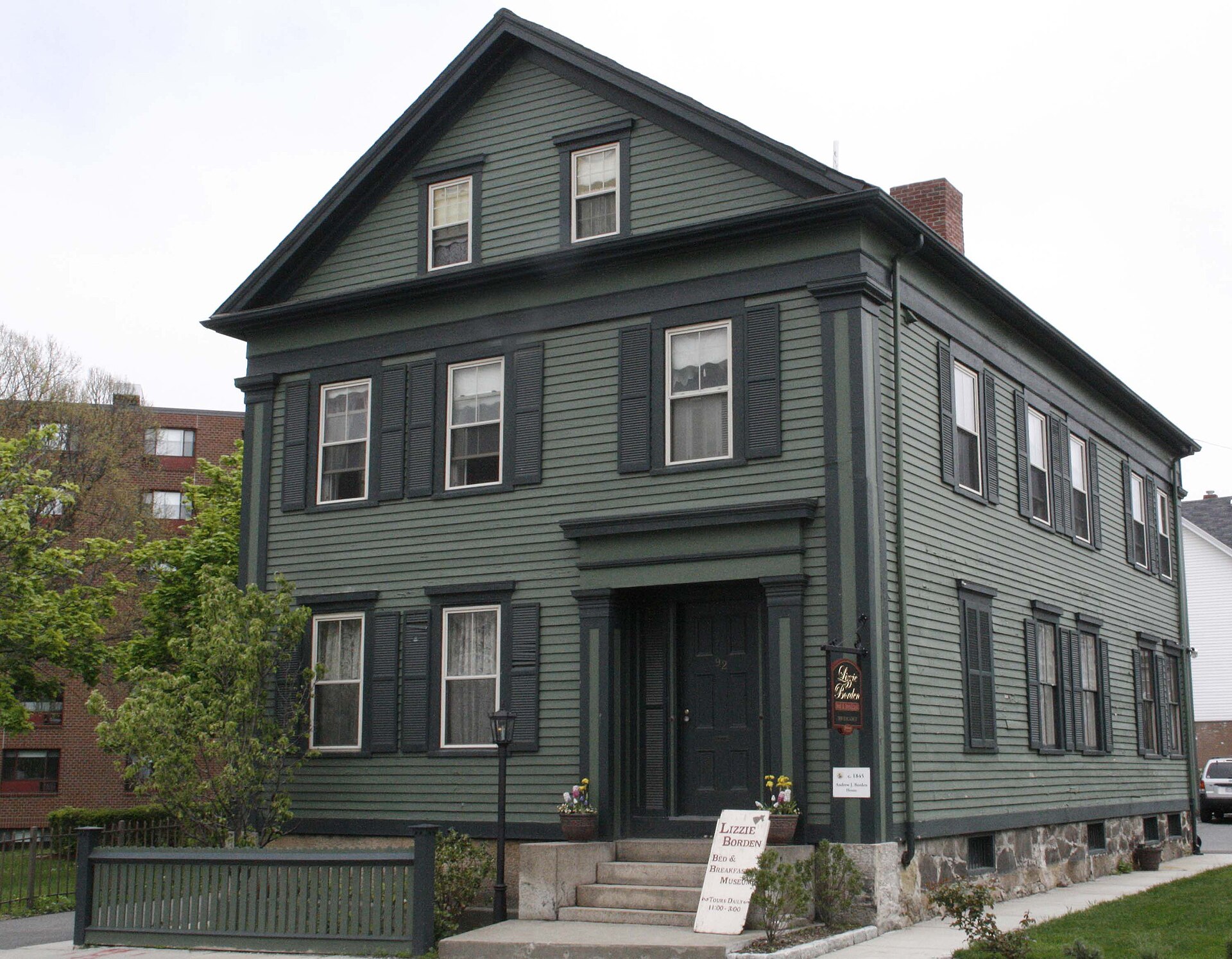 Exterior of the Lizzie Borden House, a dark green Victorian-era two-story building with black shutters and a sign reading 'Lizzie Borden Bed & Breakfast Museum.'