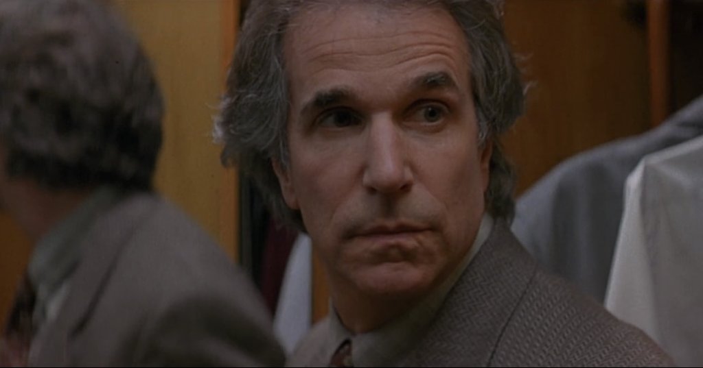Middle-aged man with graying hair in a tan blazer looking back over his shoulder with a worried expression, film still from Scream (1996).