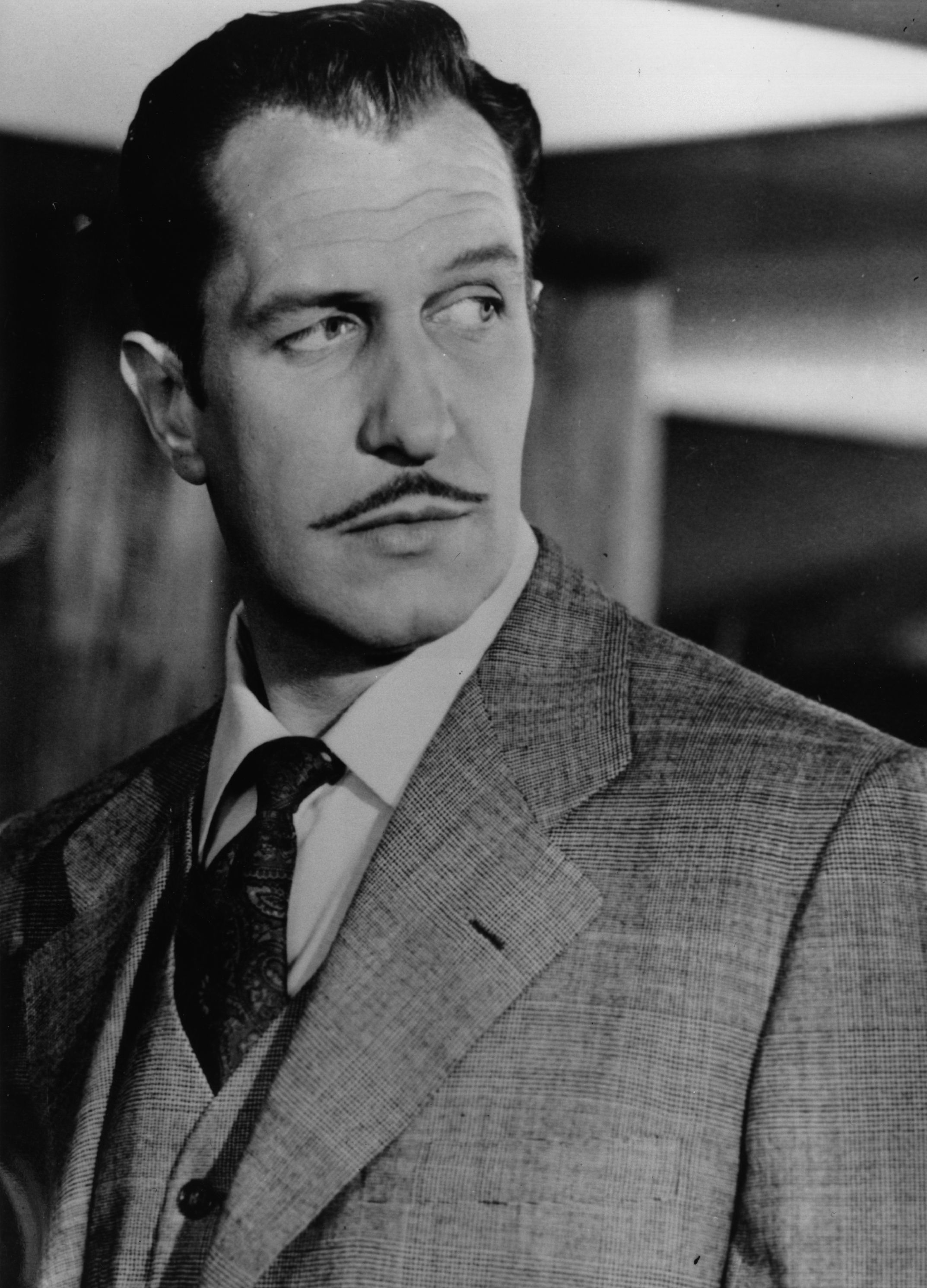 Black-and-white portrait of a mustachioed man in a tweed suit and tie, gazing sideways.