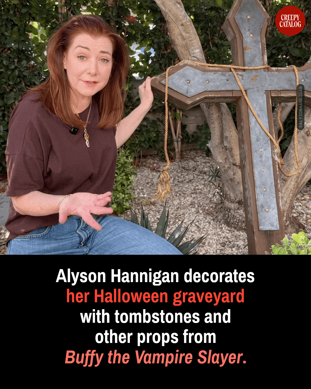 Alyson Hannigan kneeling next to a large rusted metal and wood cross prop in an outdoor garden setting.