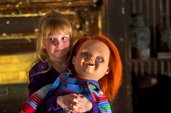 A young blonde girl hugs the Chucky Good Guy doll in a dimly lit scene from Curse of Chucky (2013).