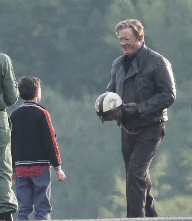 Brendan Fraser in a crash helmet seated in a vintage silver-and-red rocket car on a film set at a former military base in Suffolk, England