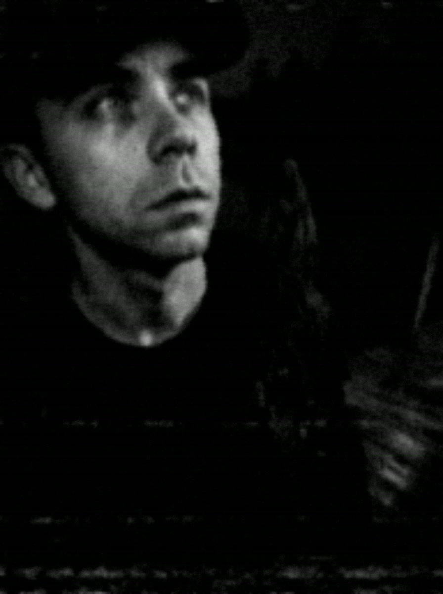 Chris Catt in a grainy black-and-white shot, wearing a cap and looking up into the dark