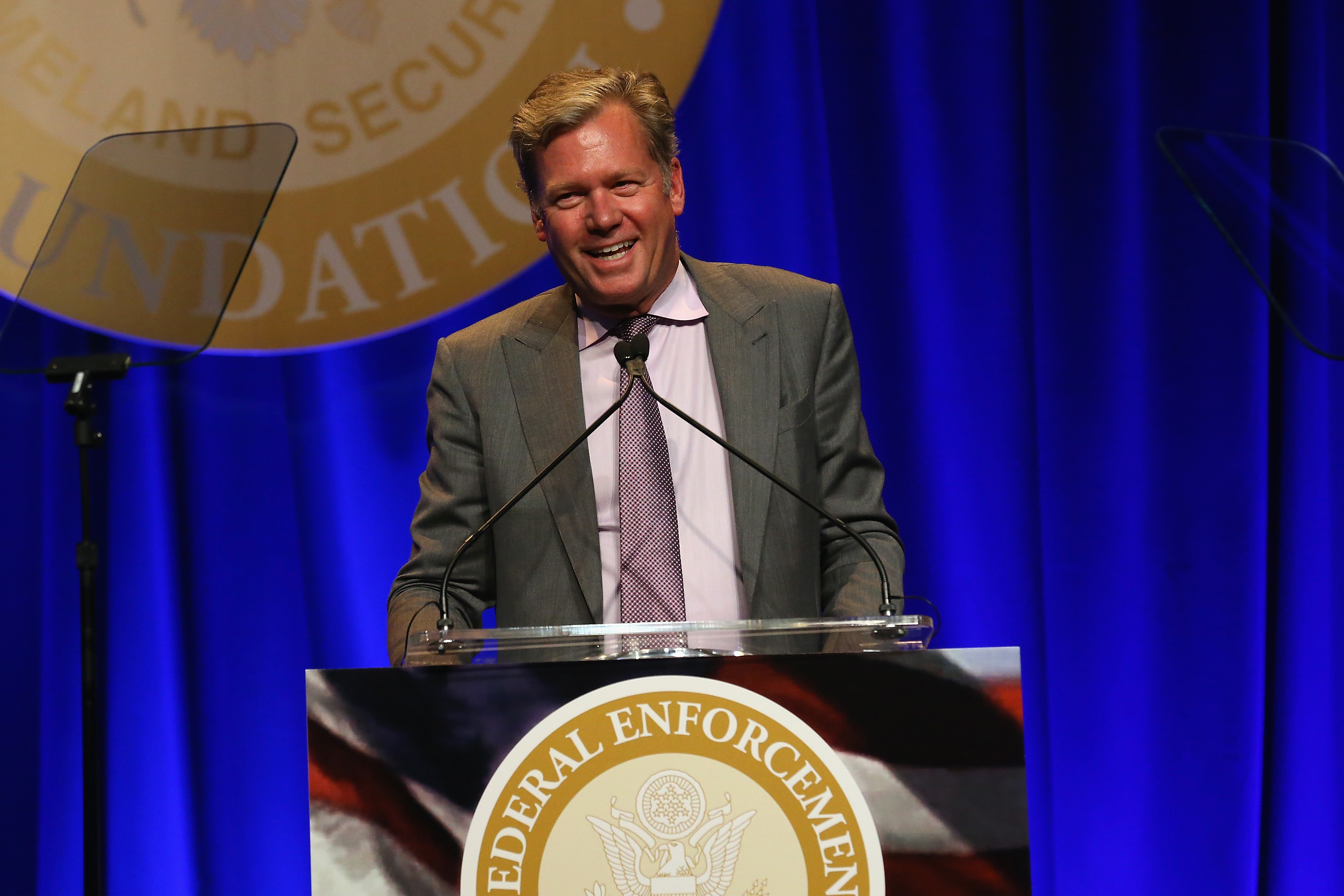 Chris Hansen smiling at a podium bearing a Federal Enforcement seal at a formal awards event.
