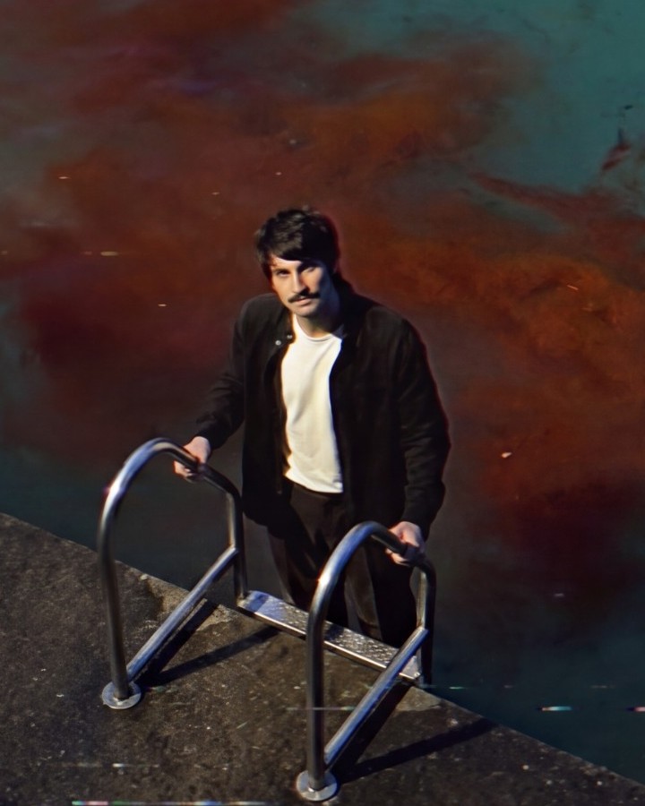Chris Lavergne standing on a pier ladder above water clouded with red