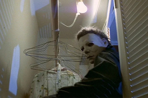 Michael Myers in a white mask crouching inside a closet among wire coat hangers, lit by a single bare bulb, from Halloween (1978).