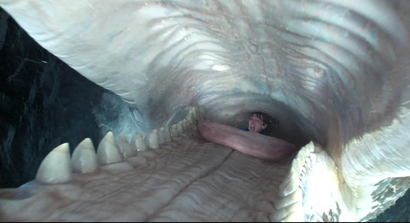 View from inside a giant creature's mouth, showing rows of teeth and a screaming person trapped at the back of the throat.