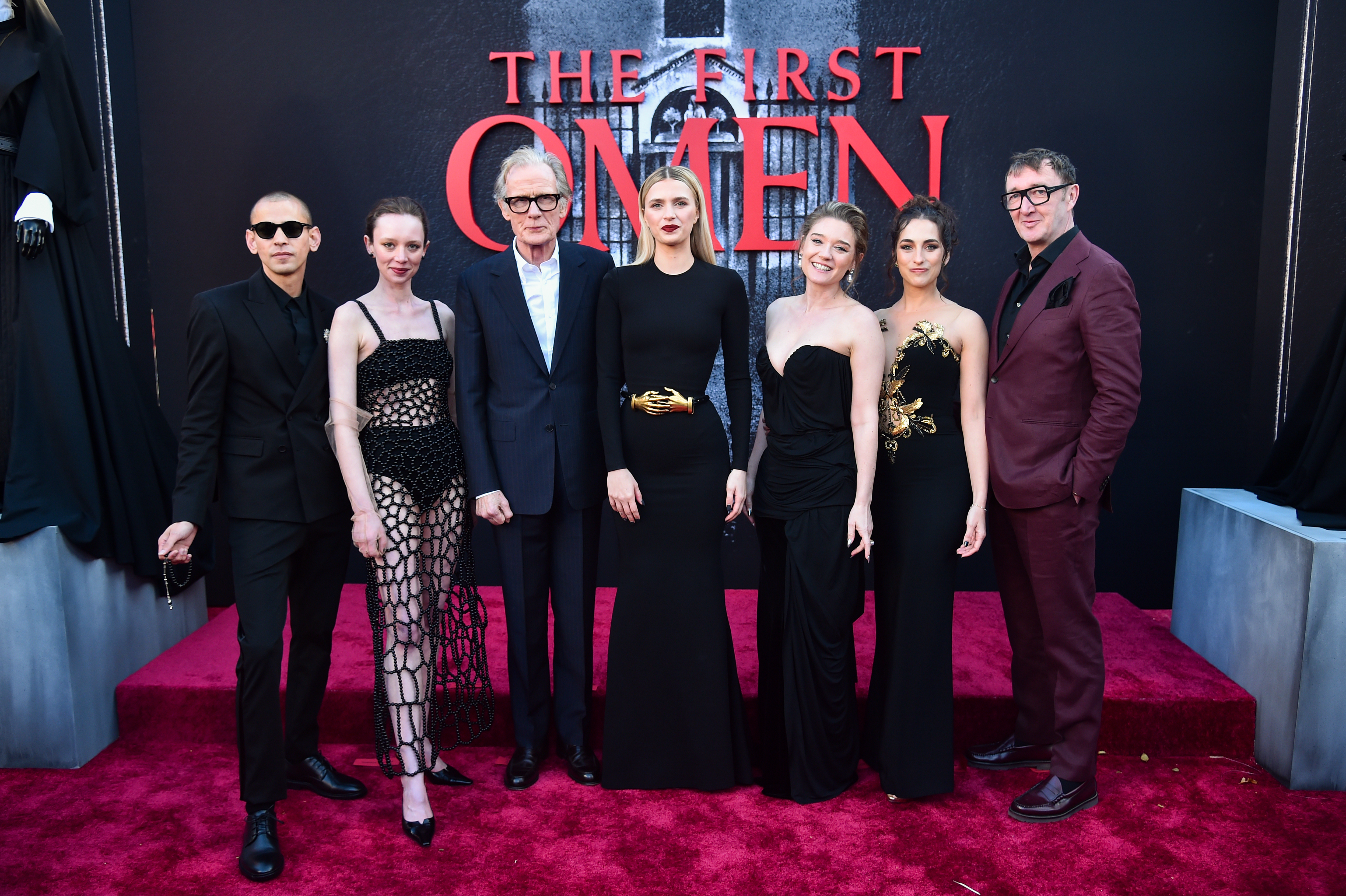 Seven cast members of The First Omen pose together on a red carpet in front of the film's backdrop at the Regency Village Theatre in Los Angeles.