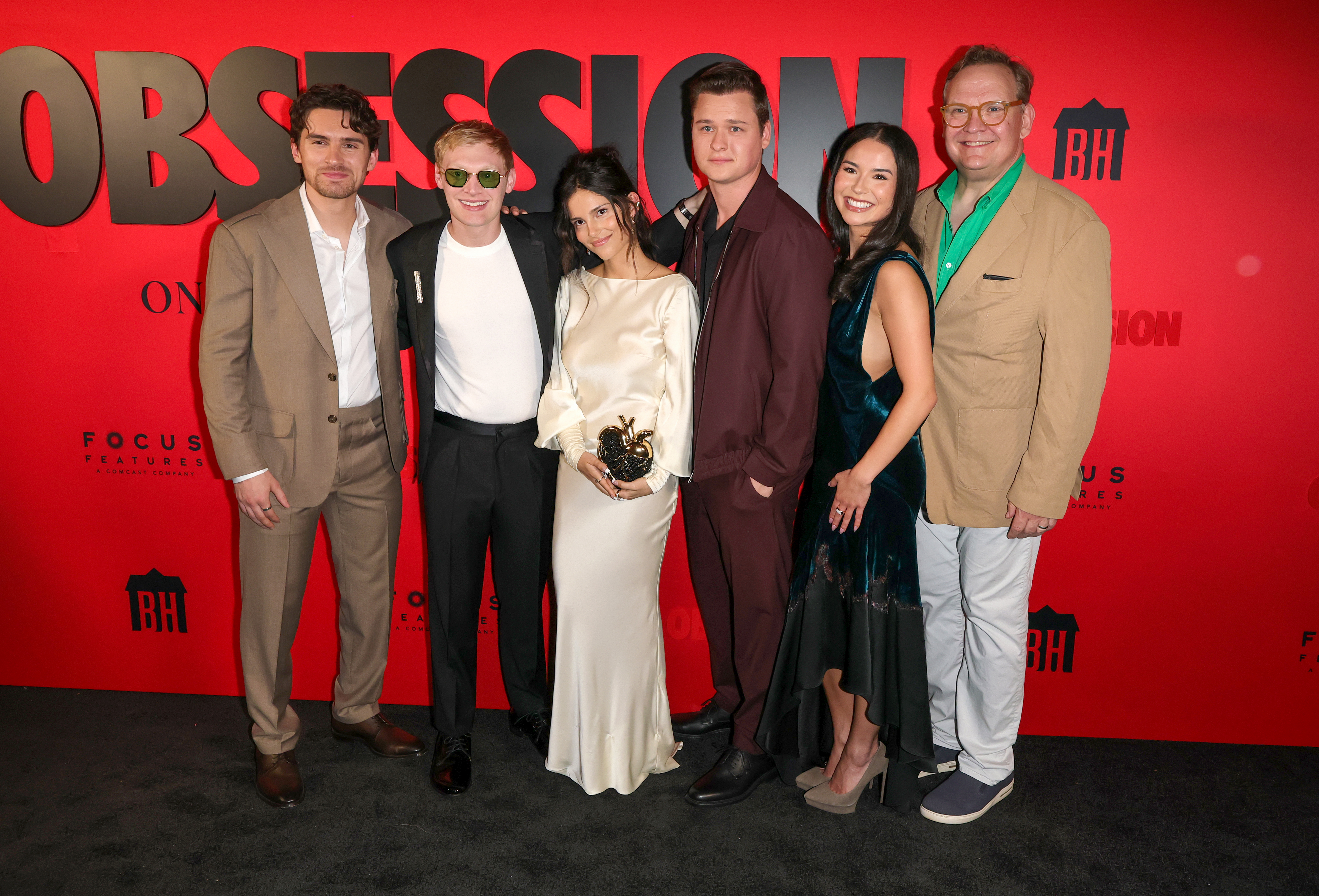 Six cast and crew members of 'Obsession' posing together on a red carpet in front of an 'Obsession' backdrop.
