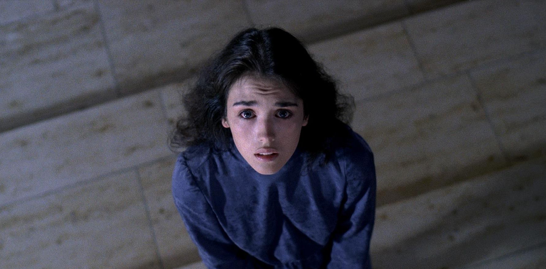 A dark-haired woman in a blue top crouches and stares upward with a fearful expression in a scene from Possession (1981).