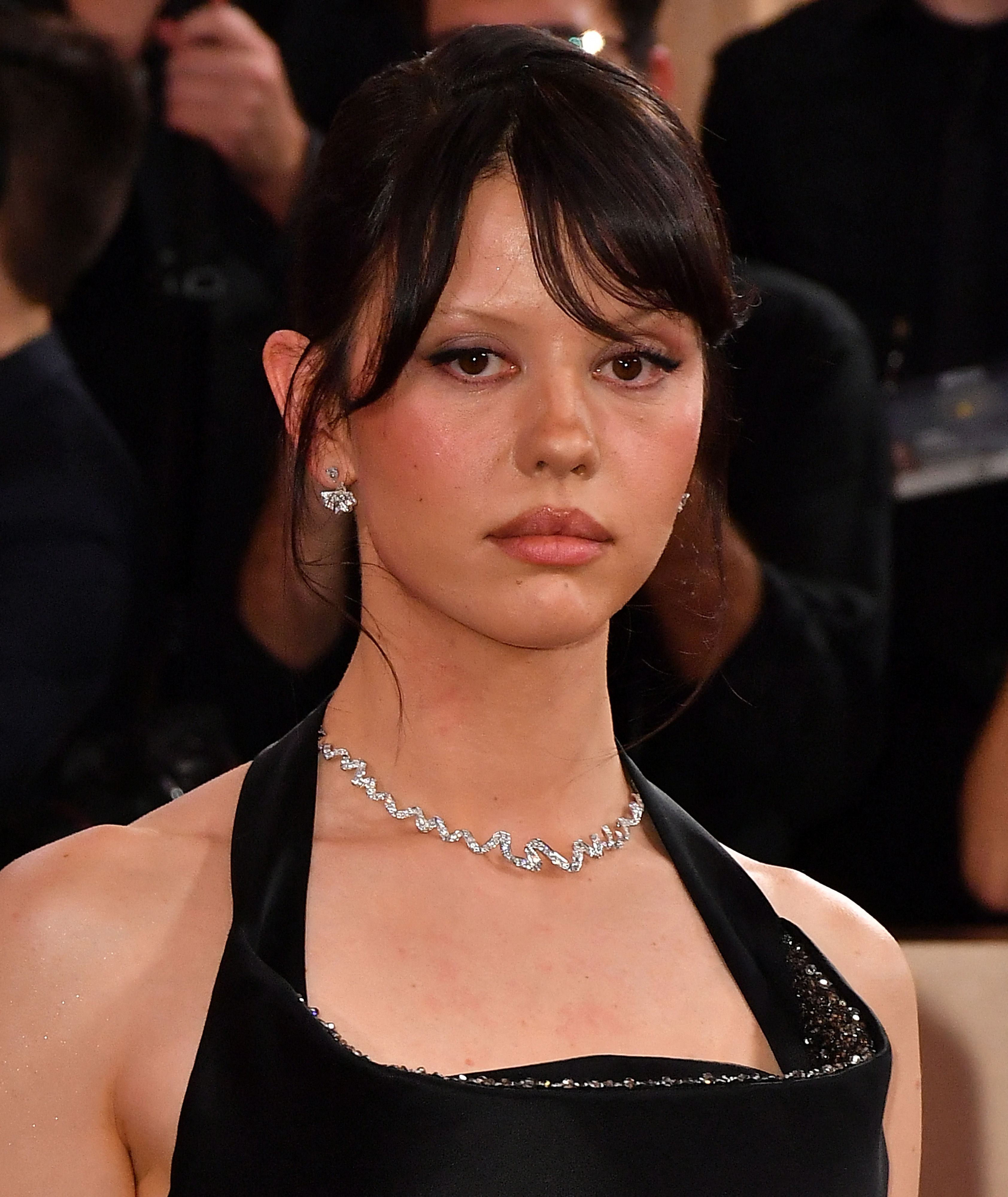 Young woman with dark hair and wispy bangs wearing a black halter dress and a diamond wave choker necklace at a formal event.