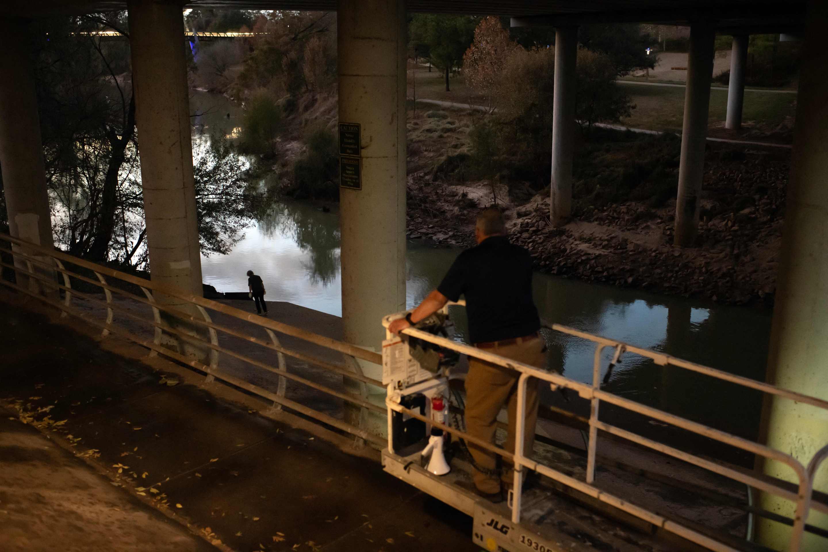 A woman crouches near a Houston bayou beneath the Waugh Bridge, scanning the ground for bats.