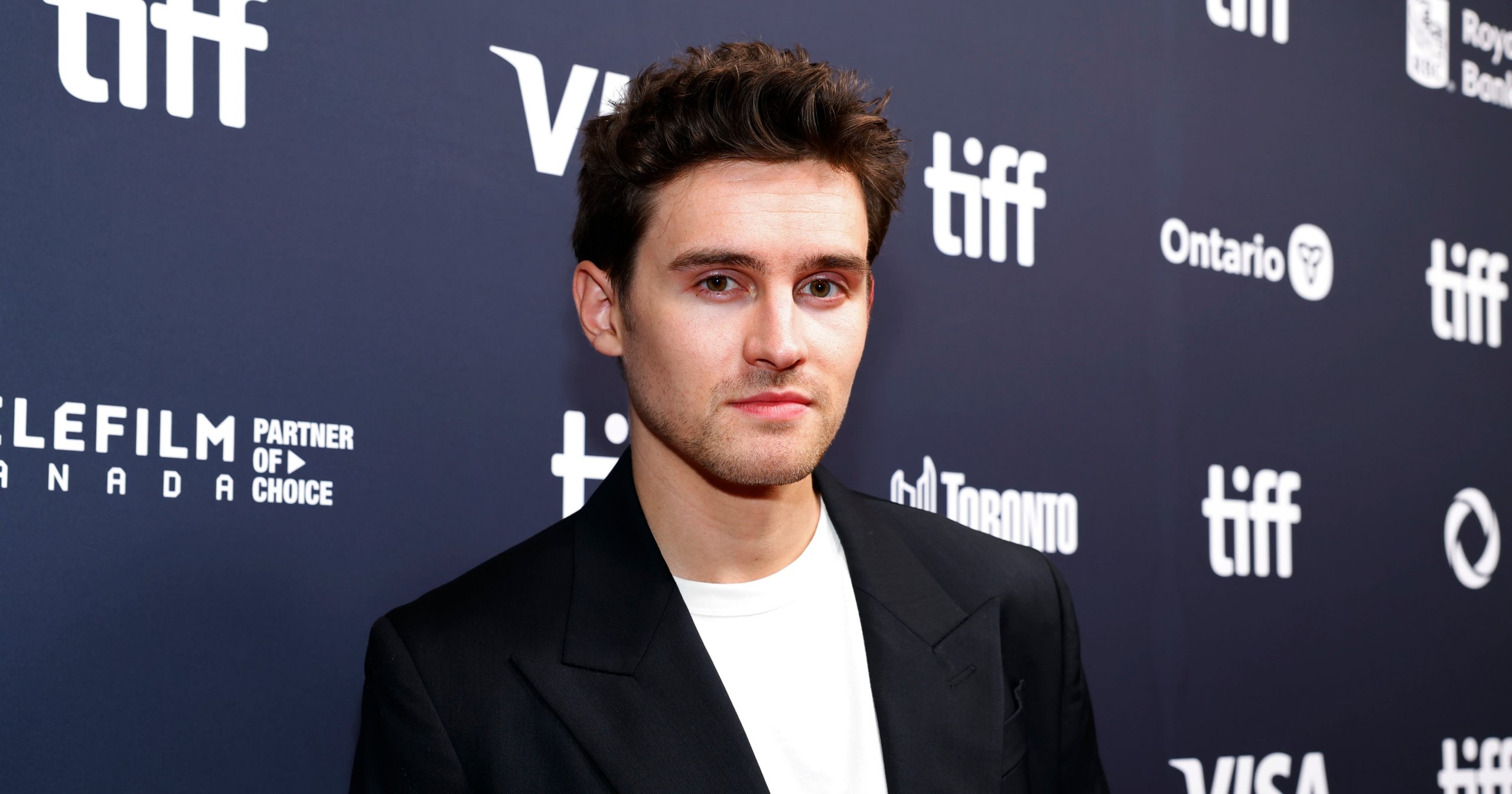 Michael Johnston in a black blazer and white t-shirt posing in front of a TIFF step-and-repeat backdrop in Toronto.