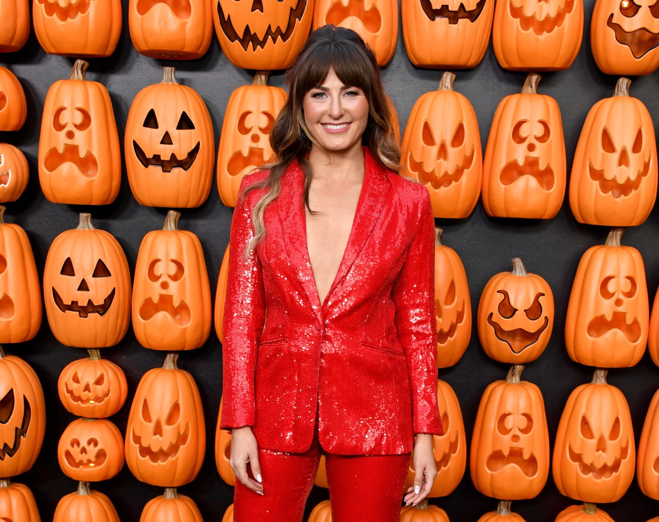 Scout Taylor-Compton smiling in a red sequin suit in front of a wall of carved jack-o'-lanterns at the Halloween Ends premiere.