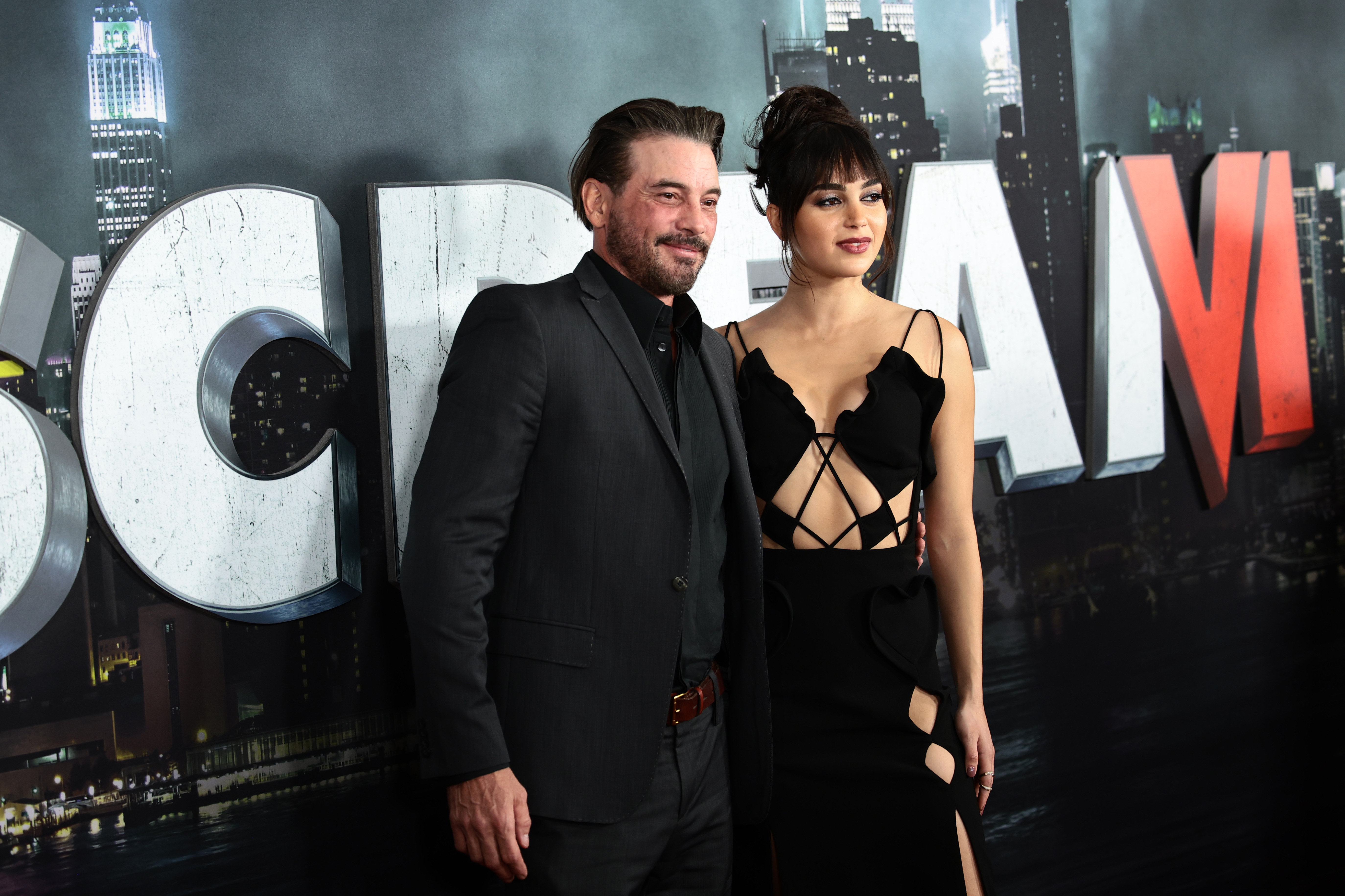 Skeet Ulrich in a dark suit and Melissa Barrera in a black cutout gown pose at the Scream VI world premiere red carpet.