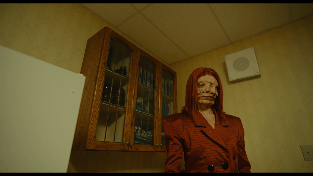 Red-haired distorted Still Life character from the Backrooms film, recreated with prosthetic makeup